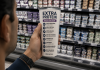Estamos comprando Salud? Hombre observa un yogur con múltiples beneficios nutricionales en un supermercado, reflexionando sobre cómo entendemos la salud